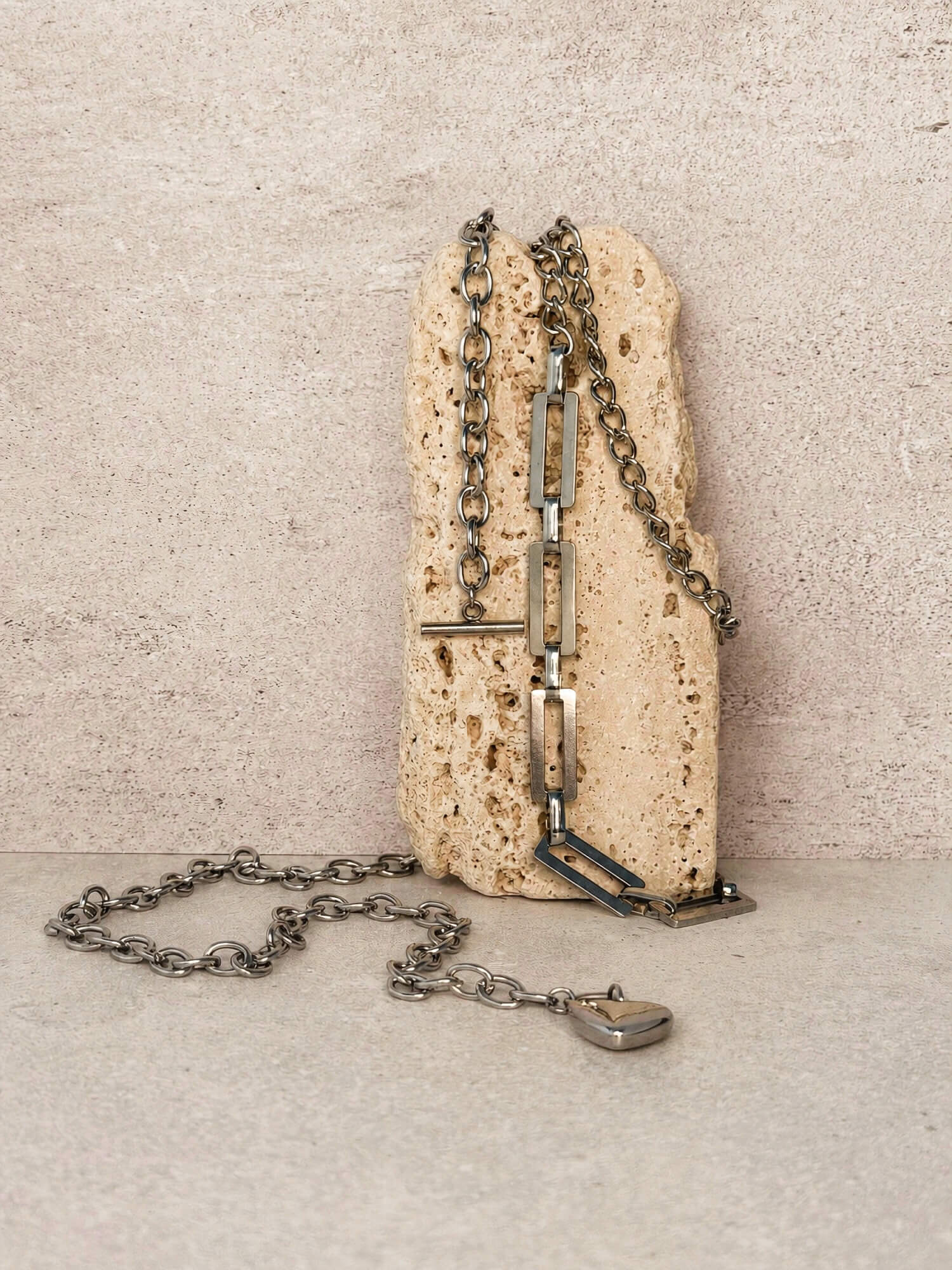 Silver curb chain necklace and rectangular link necklace with heart charm styled on stone