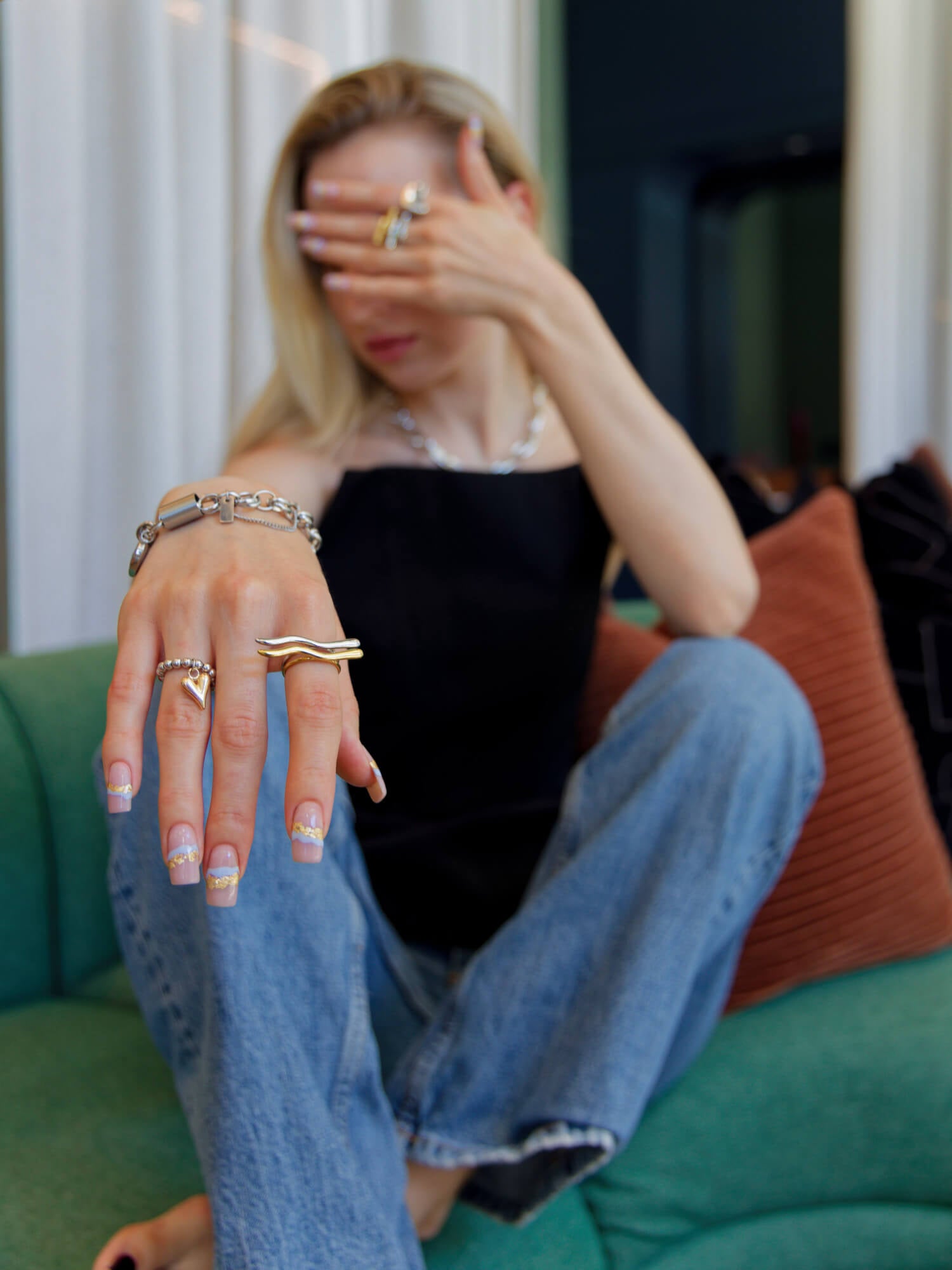 Lifestyle photo of a model wearing layered silver and gold jewelry, including a statement bracelet, rings and chain necklace by Alvijo.