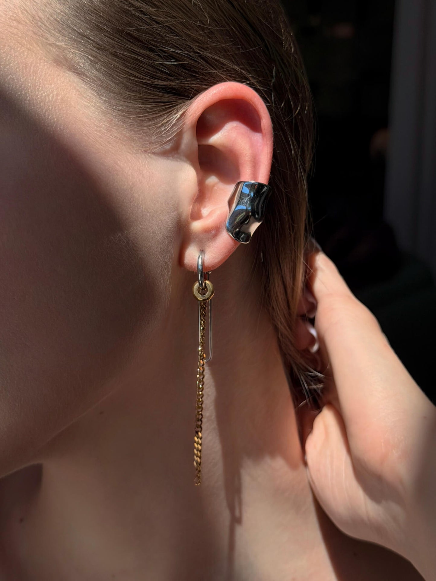 Model wearing a convertible chain and heart earrings and a chunky silver ear cuff