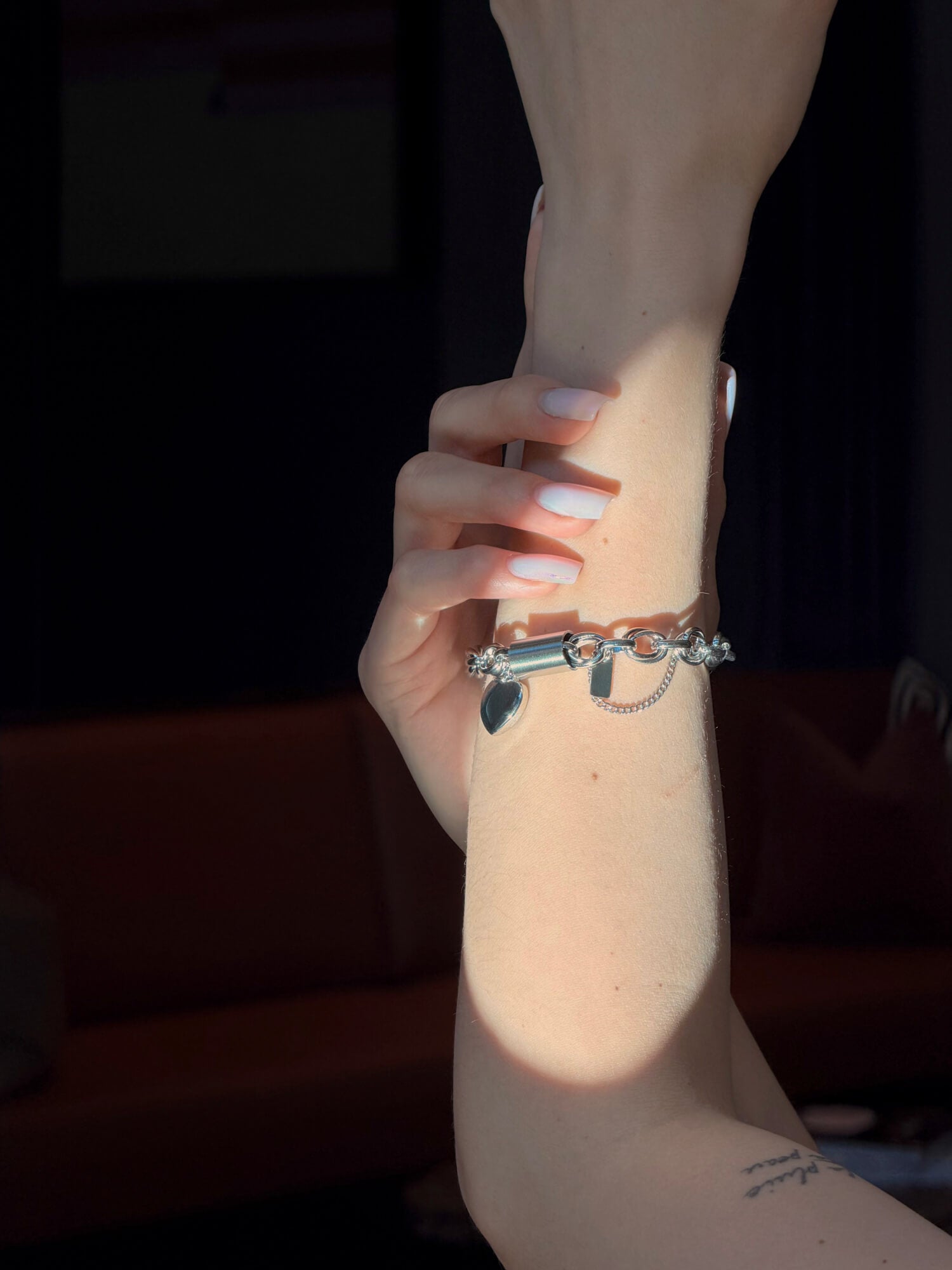 Close-up of a wrist wearing a silver bracelet with charms against a dark background