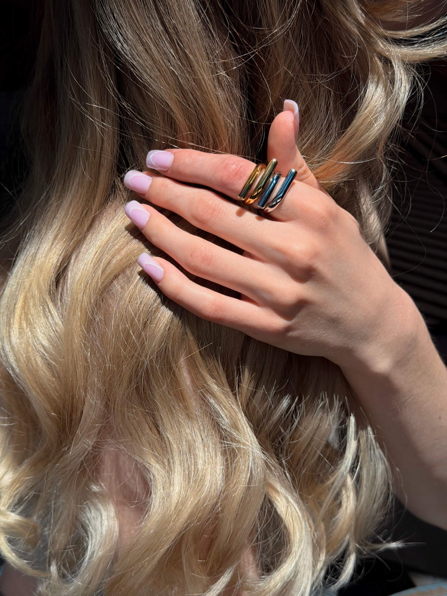 Model wearing sculptural wrap gold ring and silver ring on finger