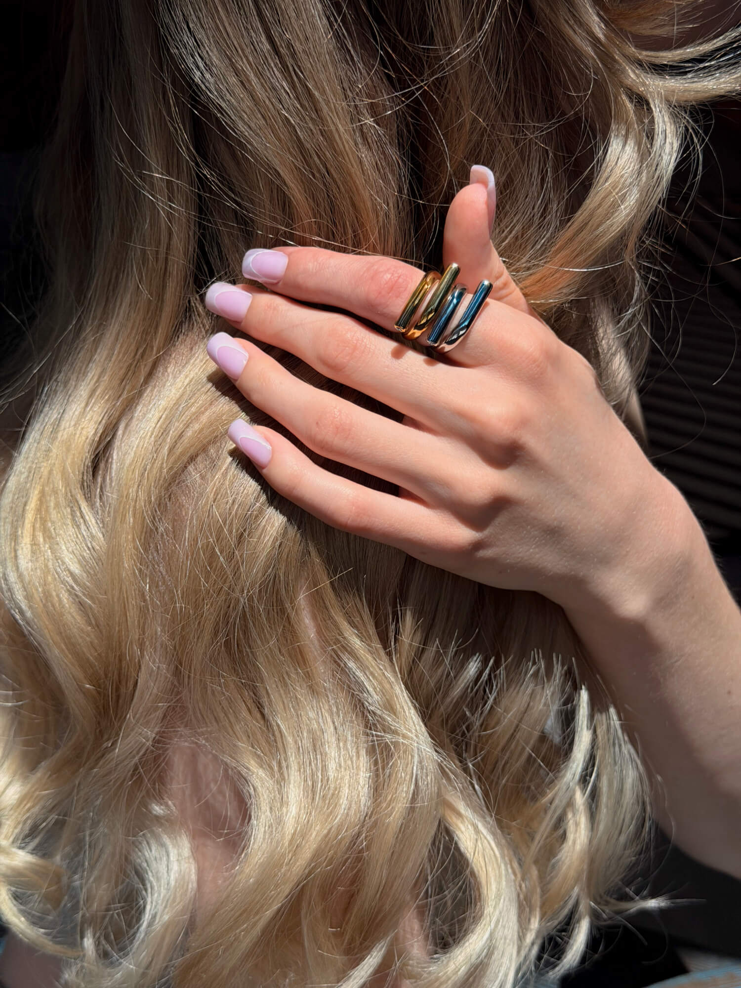 Model wearing sculptural wrap gold ring and silver ring on finger
