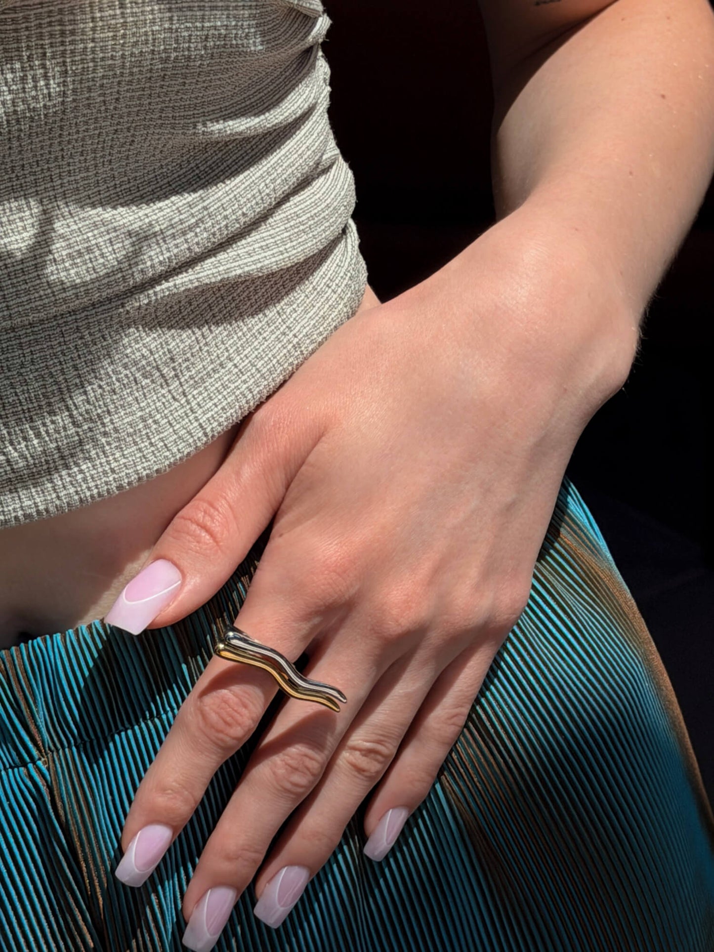 Model wearing culptural gold and silver rings, wave design